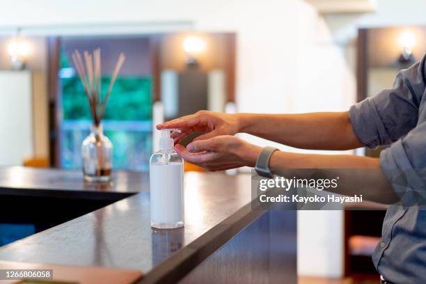 an asian man disinfecting his hands with antiseptic gel at the shop counter. - lockdown haircut stock pictures, royalty-free photos & images