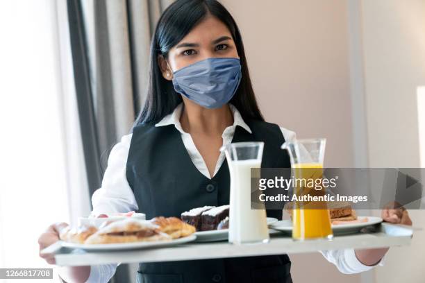 portrait of a latin woman waitress wearing face mask, serving breakfast at hotel room - quarantine stock pictures, royalty-free photos & images