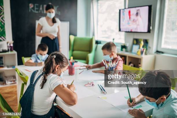 children with protective face masks drawing in preschool - preschool stock pictures, royalty-free photos & images