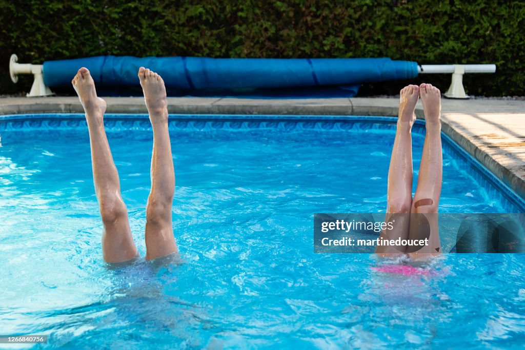 Two preteen girl's legs standing up in pool.