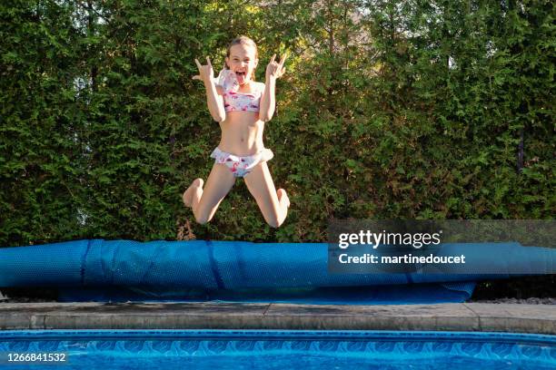 preteen girl jumping in backyard pool making a face. - preteen girl swimsuit stock pictures, royalty-free photos & images