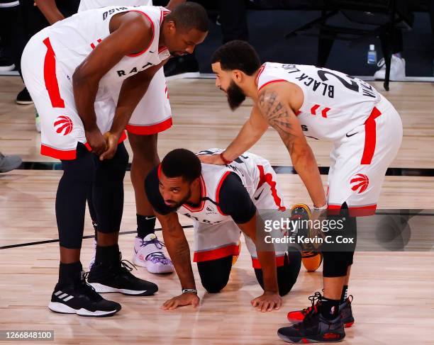 Norman Powell of the Toronto Raptors is helped up by teammates Serge Ibaka and Fred VanVleet against the Brooklyn Nets during the first quarter in...