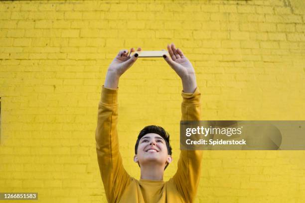 de jonge vrouw in geel neemt een selfie voor gele muur van de baksteen - breaking through wall stockfoto's en -beelden