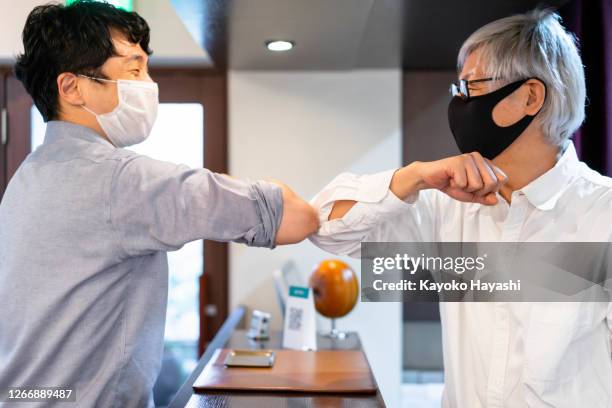 a male clerk and a male customer greet each other at each other's elbows inside a beauty salon during the corona crisis. - covid handshake stock pictures, royalty-free photos & images