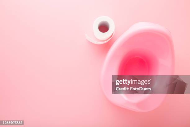 Baby potty and white toilet paper roll on light pink table background. Pastel color. Hygiene concept. Closeup. Empty place for text. Top down view.