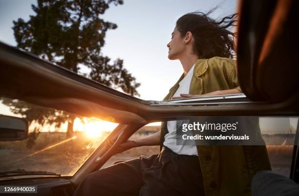 young latina woman leaning out of car window sitting on car door at sunset - wind in face stock pictures, royalty-free photos & images