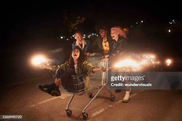 multiethnic group of friends having fun with shopping cart and sparklers - sparkler imagens e fotografias de stock