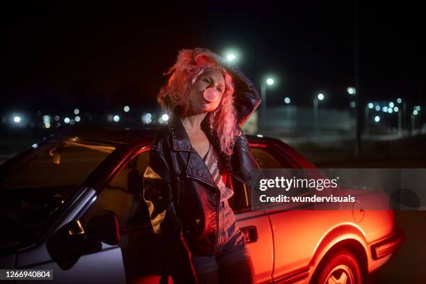 chica joven alternativa apoyada en el coche con goma de mascar por la noche - punk person fotografías e imágenes de stock