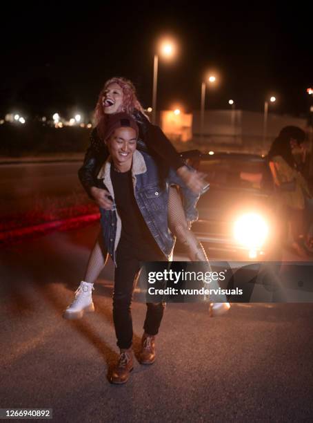 young man giving girlfriend piggyback ride at night on parking lot - piggyback stock pictures, royalty-free photos & images