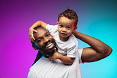 African-american father and son portrait on gradient studio background in neon