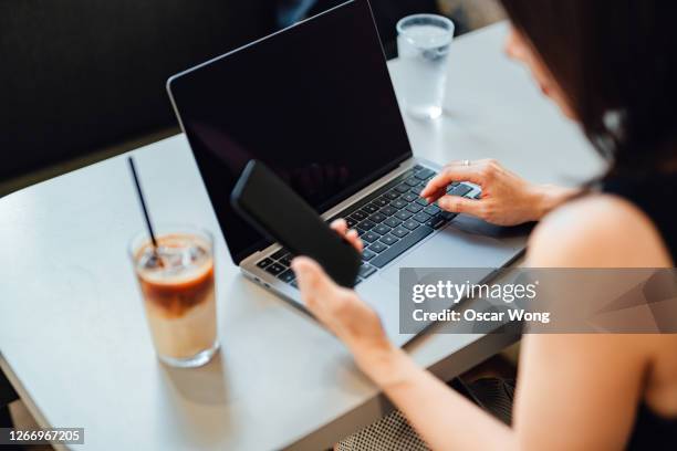 freelancer using smart phone while working with laptop at cafe - working on laptop back stock pictures, royalty-free photos & images