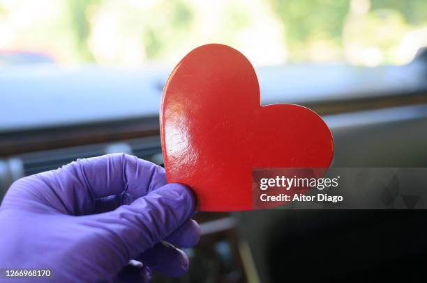 person's hand with protective gloves holding a red heart shape inside a car. - arret cardiaque photos et images de collection