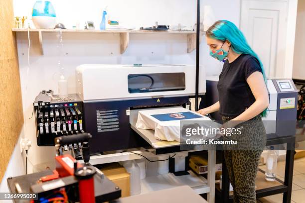 lavoratrice moderna che guarda il risultato della stampa di t-shirt nella macchina serigrafica ed è stupita dai risultati - print foto e immagini stock