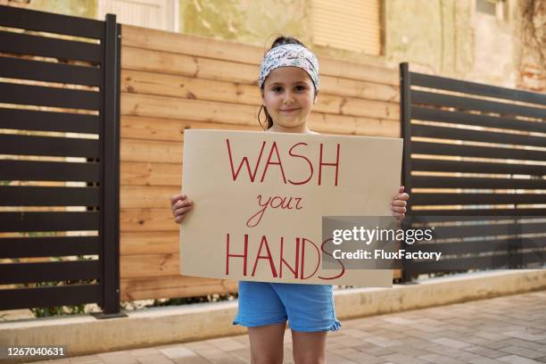 cute smiling girl holding a wash your hands sign on a city street - state of emergency sign stock pictures, royalty-free photos & images