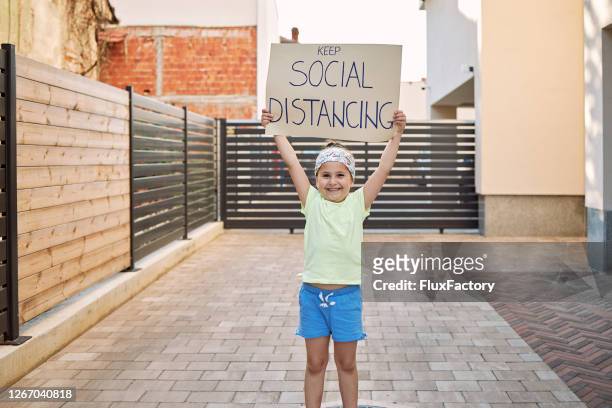 young female child holding a keep social distancing sign during coronavirus epidemic - keep out sign imagens e fotografias de stock
