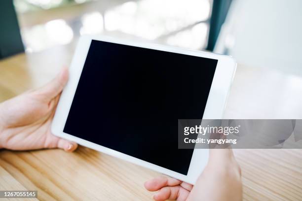 mockup image of hands holding white tablet pc with blank black desktop screen on wooden table - tablet pc stock-fotos und bilder