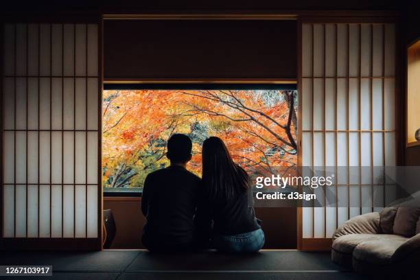 a loving young asian couple sitting side by side by the window in a traditional japanese style apartment, chatting and enjoying the beautiful nature autumn scenics during the day - japanese culture stockfoto's en -beelden