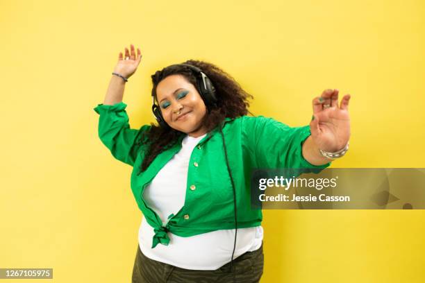 young woman with headphone dances in front of a yellow background - plus size fashion model stock pictures, royalty-free photos & images