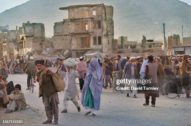 Busy street scene with women dressed in niqabs, and men wearing Afgan lungee turbans, with damaged buildings in the background, Afghanistan, 1996....