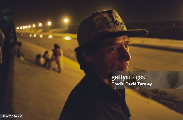 Mexican man wearing a baseball cap on a flood-control channel as night falls over the border between Mexico and California in the United States,...