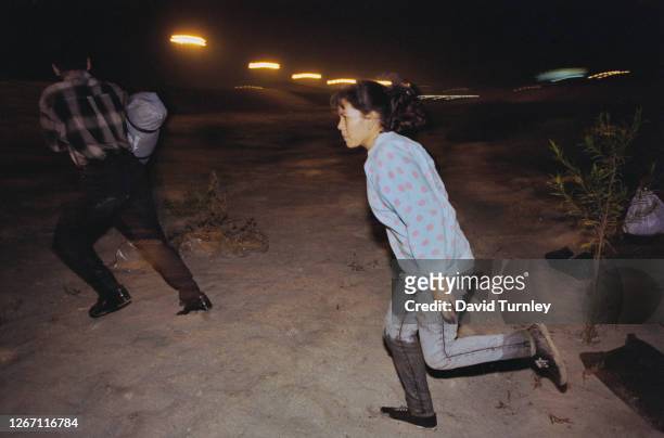Mexcian man and woman running under cover of darkness as night falls over the border as they look to cross from Mexico into California in the United...