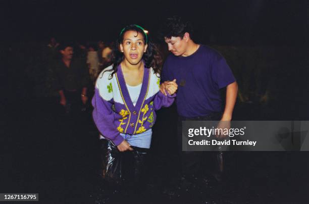 Young Mexican couple holding hands as night falls over the border as they look to cross from Mexico into California in the United States, 1993.