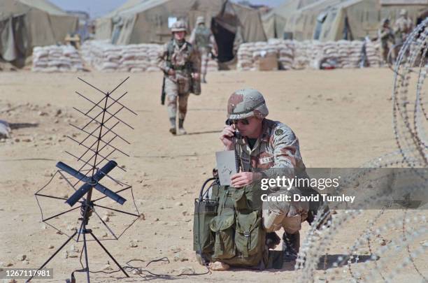 Member of the US Military wearing military fatigues and using a field telephone, an aerial at his wide and sandbags in the background, during the...