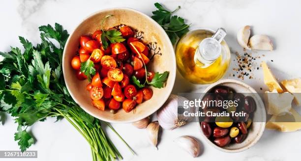 food ingredients (cherry tomatoes, parsley, garlic, parmesan cheese, olives, and olive oil) on white background - dieta mediterranea foto e immagini stock