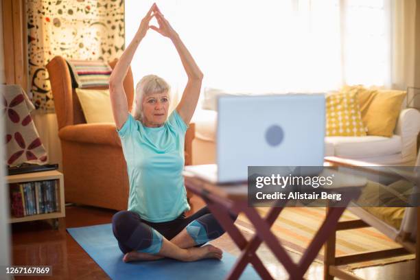 senior woman doing yoga with an on-line tutorial from her laptop during covid lockdown - learning agility stock pictures, royalty-free photos & images