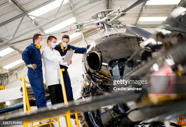 group of mechanics wearing facemasks at work while doing an inspection on a helicopter - biosecurity stock pictures, royalty-free photos & images