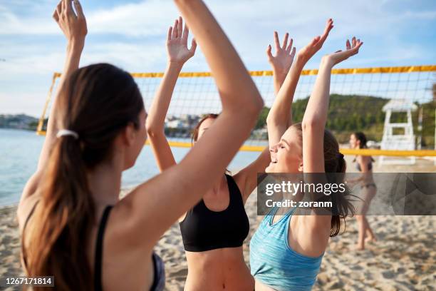 drei junge frauen heben die arme für high-five nach dem tor in beachvolleyball-spiel - womens beach volleyball stock-fotos und bilder