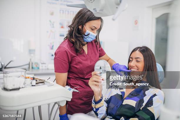 happy female patient looking at mirror her white teeth after dental work - dentist's chair stock pictures, royalty-free photos & images