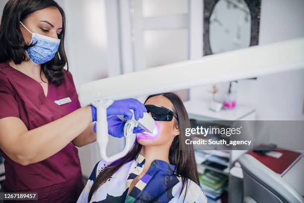 giovane donna sottoposta a trattamento di sbiancamento dei denti laser presso l'ordinazione del dentista - sbiancamento dentale foto e immagini stock