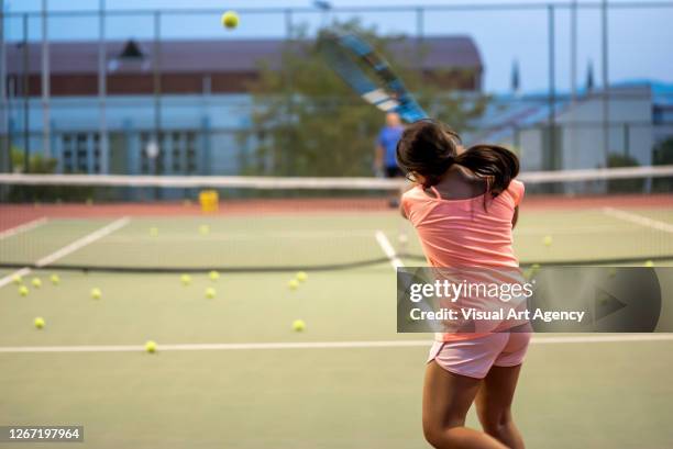 a girl is shooting backhand to her coach on the hardcourt focus on foreground - tennis ball on court stock pictures, royalty-free photos & images