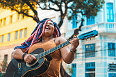 Woman with rastafarian hair style playing acoustic guitar on the street