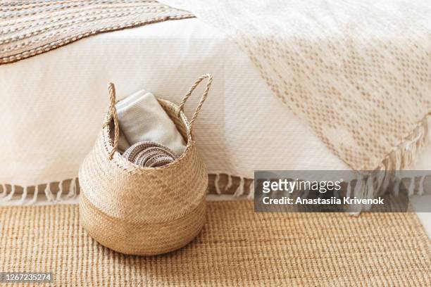 folded gray knitted plaid in straw basket on wicker carpet near bed. cozy hygge home style. fall winter season concept. close up, copy space. - bedclothes stock-fotos und bilder