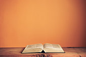 Open Holy Bible on a old wooden table. Beautiful orange wall background.