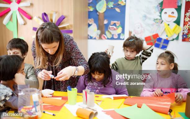 fröhliche schulkinder mit besonderen bedürfnissen sitzen am schreibtisch in der grundschulklasse - children in need stock-fotos und bilder