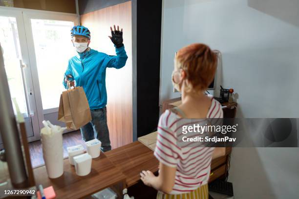 delivery man leaving a fast food restaurant with freshly made meals and waving to a female employee as he walking out the door - leaving restaurant stock pictures, royalty-free photos & images