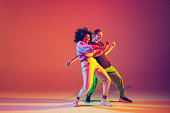 Stylish man and woman dancing hip-hop in bright clothes on gradient background at dance hall in neon light