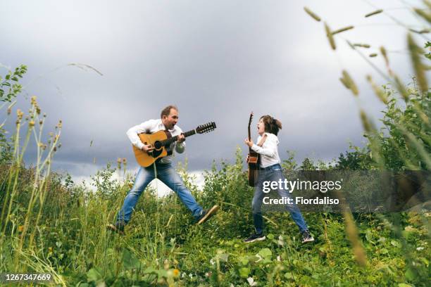 father and son with guitars in white shirts and jeans play rock and roll outdoors - músico de rock imagens e fotografias de stock