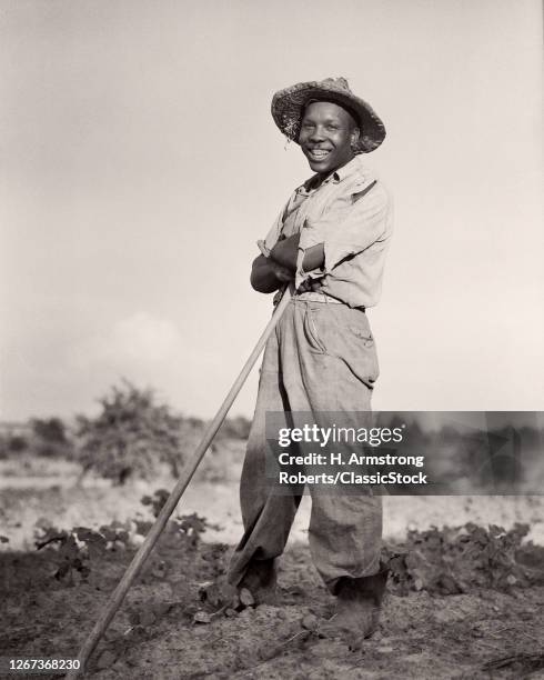 1930s Smiling African-American Man Tobacco Farmer Wearing Straw Hat Standing Leaning On Hoe Looking At Camera North Carolina USA