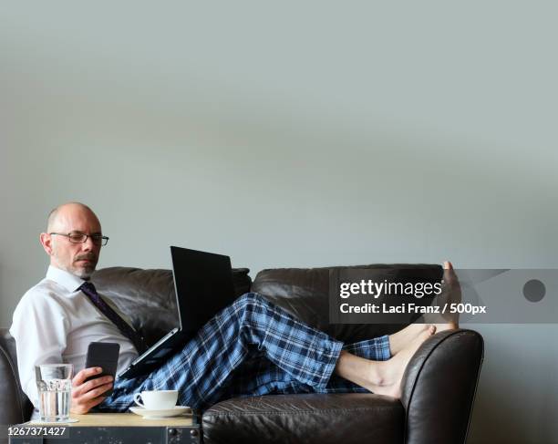 businessman working from home on couch in dress shirt and pyjama pants with laptop and mobile smartphone, stuttgart, germany - pyjamas stock pictures, royalty-free photos & images