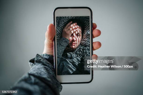 cropped hands of woman holding mobile phone while taking selfie against grey background - self portrait photography stock pictures, royalty-free photos & images