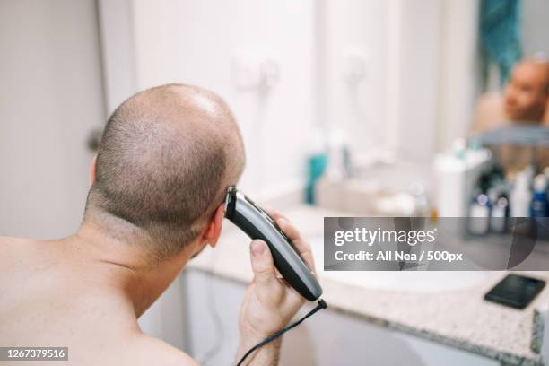 man shaving his head with electric razor in bathroom, lleida, spain - head shave stockfoto's en -beelden