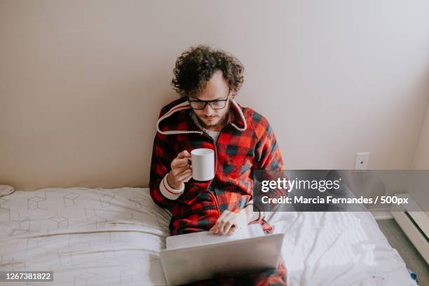 man drinking coffee while on laptop and sitting on bed at home, victoria, canada - pajamas stock pictures, royalty-free photos & images