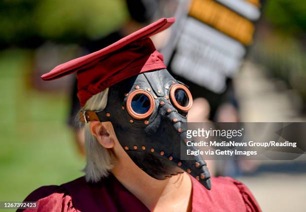 Kutztown, PA A protester, wearing a plague doctor mask with a beak, a graduation gown, and mortarboard. On Main Street in Kutztown outside the...