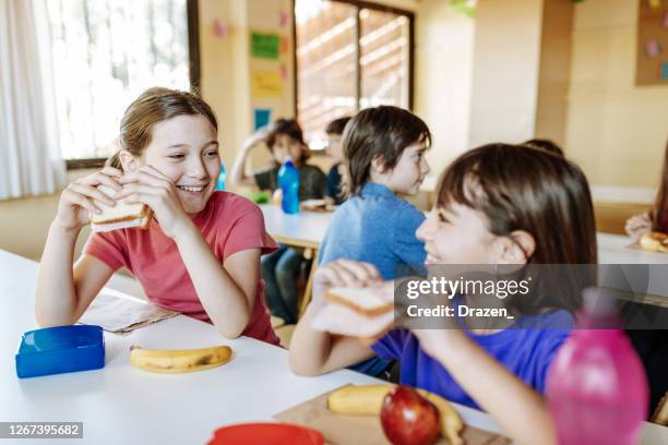 ragazze delle scuole elementari che mangiano panini durante la pausa - girls laughing eating sandwich foto e immagini stock
