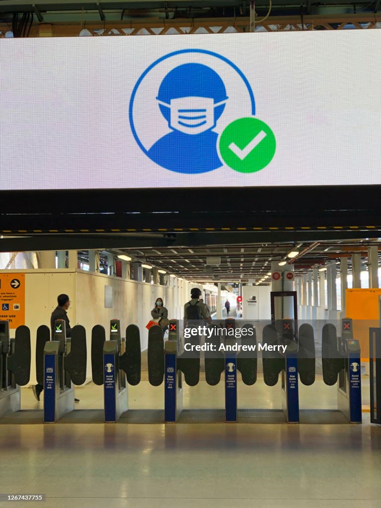 Large COVID-19 wear mask sign above train station ticket barrier