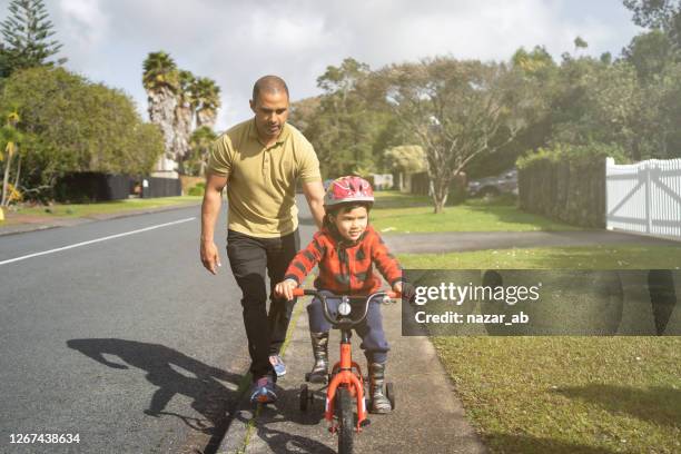 father supporting son to lean bike. - new zealand family stock pictures, royalty-free photos & images